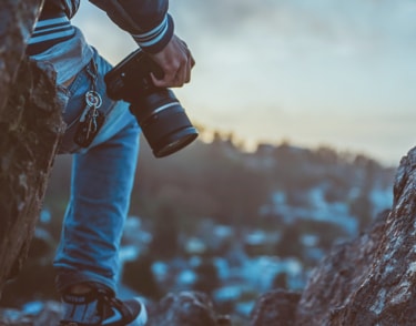 Person holding a camera outdoors, with a blurred city skyline in the background.
