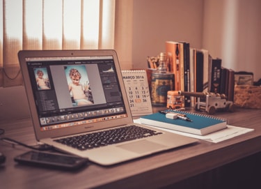 Open laptop displaying photo editing software with a baby photo, next to a desk with books, a calendar, and notepad.