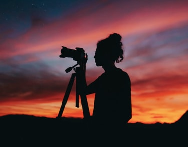 Silhouette of a person holding a camera on a tripod at sunset.